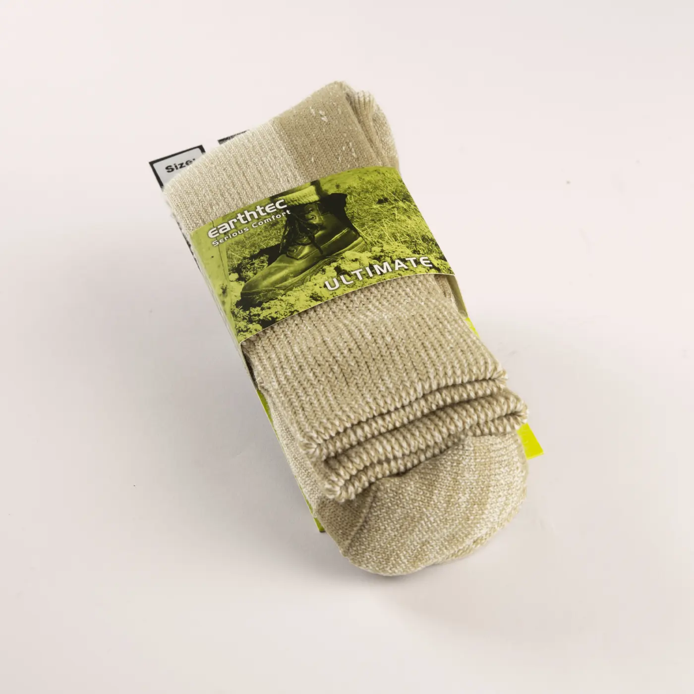 A pair of beige Earthtec Ultimate socks is neatly folded and wrapped in packaging featuring a photo of boots on grass. The socks have visible ribbed cuffs and a soft, textured appearance.
