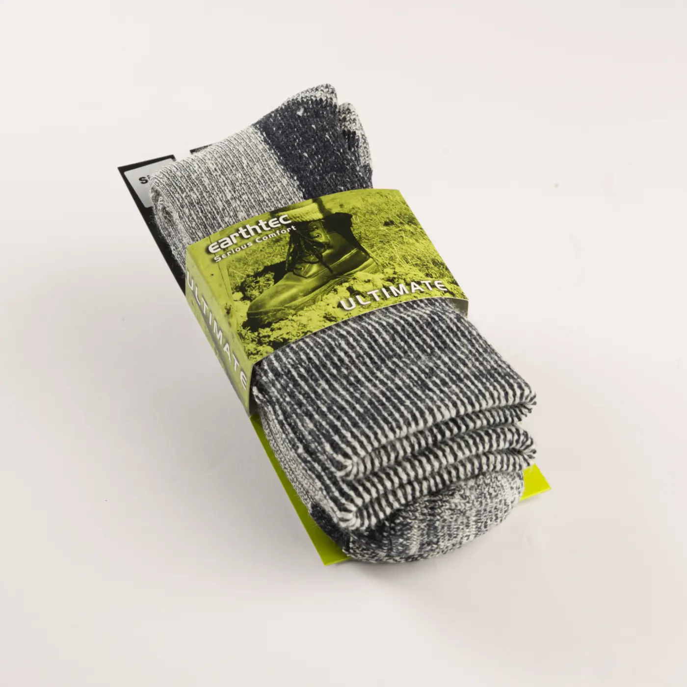 A folded pair of gray and black striped socks is wrapped in green packaging labeled earthtec and Ultimate. The packaging shows a picture of a boot and outdoor scenery.