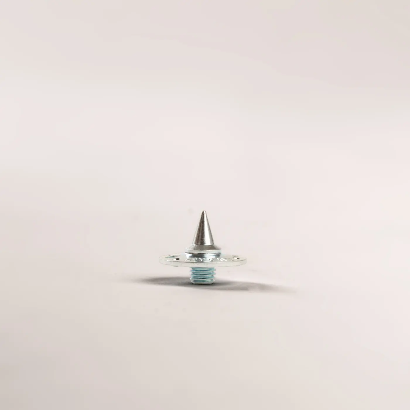 A single metal screw with a pointed, conical tip and a washer is standing upright on a plain light-colored background.