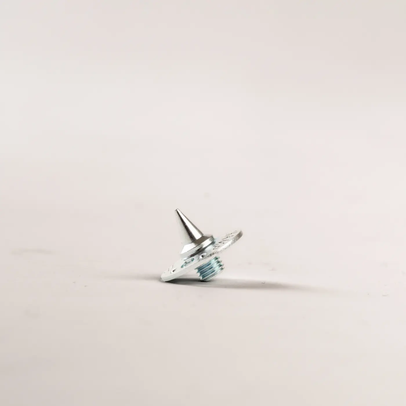 A small metal screw with a pointed tip and a thin washer rests on a plain, light-colored surface, casting a soft shadow.