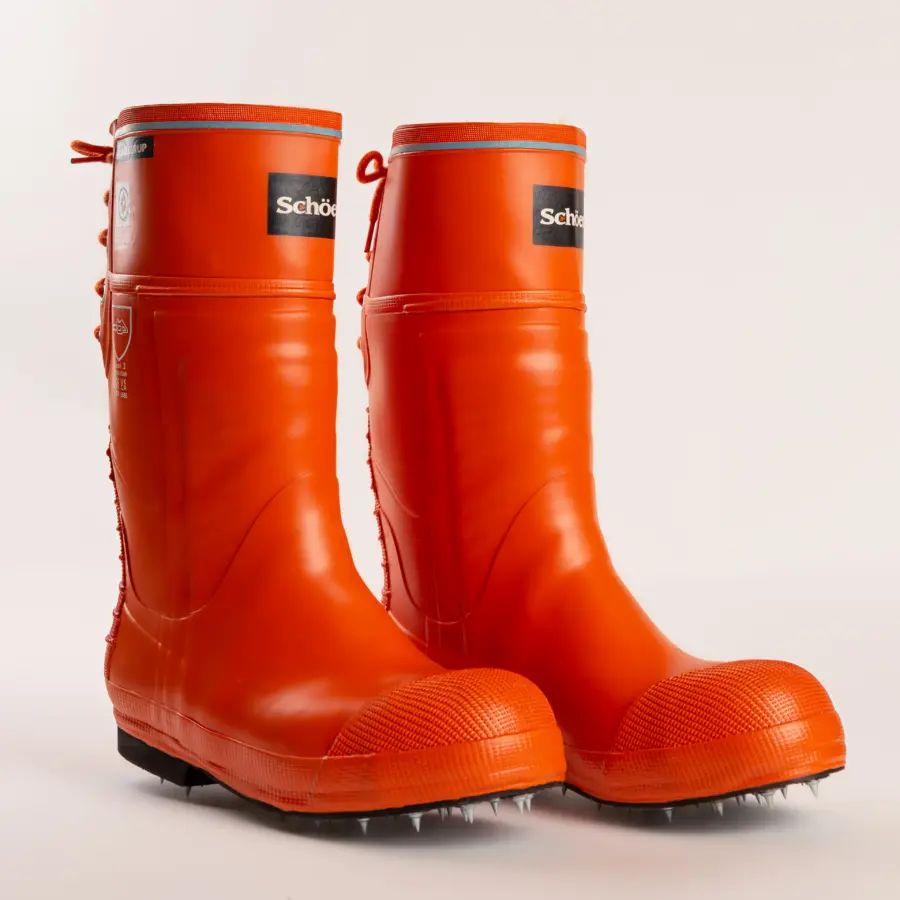 A pair of bright orange rubber boots with black soles and visible metal spikes underneath. The boots have laces at the back and a “Schütze” label on the front. The background is plain white.