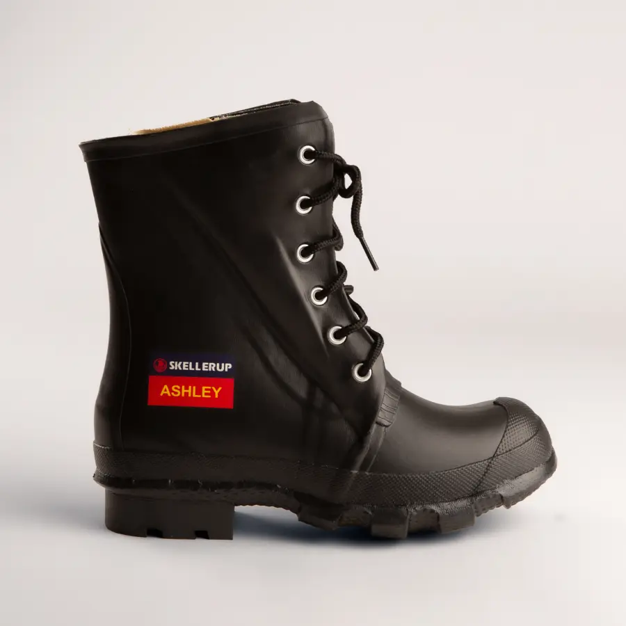 A black rubber lace-up work boot with rugged soles and metal eyelets, featuring a label that reads SKELLERUP ASHLEY on the side, displayed against a plain white background.