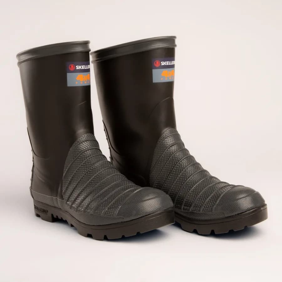 A pair of black rubber work boots with textured, reinforced fronts and thick soles, placed side by side on a light background. Labels reading Skeiler and 4x4 are visible near the top of each boot.