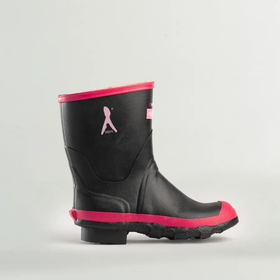 A black rubber rain boot with pink trim around the sole and top. The boot features a pink ribbon emblem on the side, symbolizing breast cancer awareness. The background is plain and light-colored.