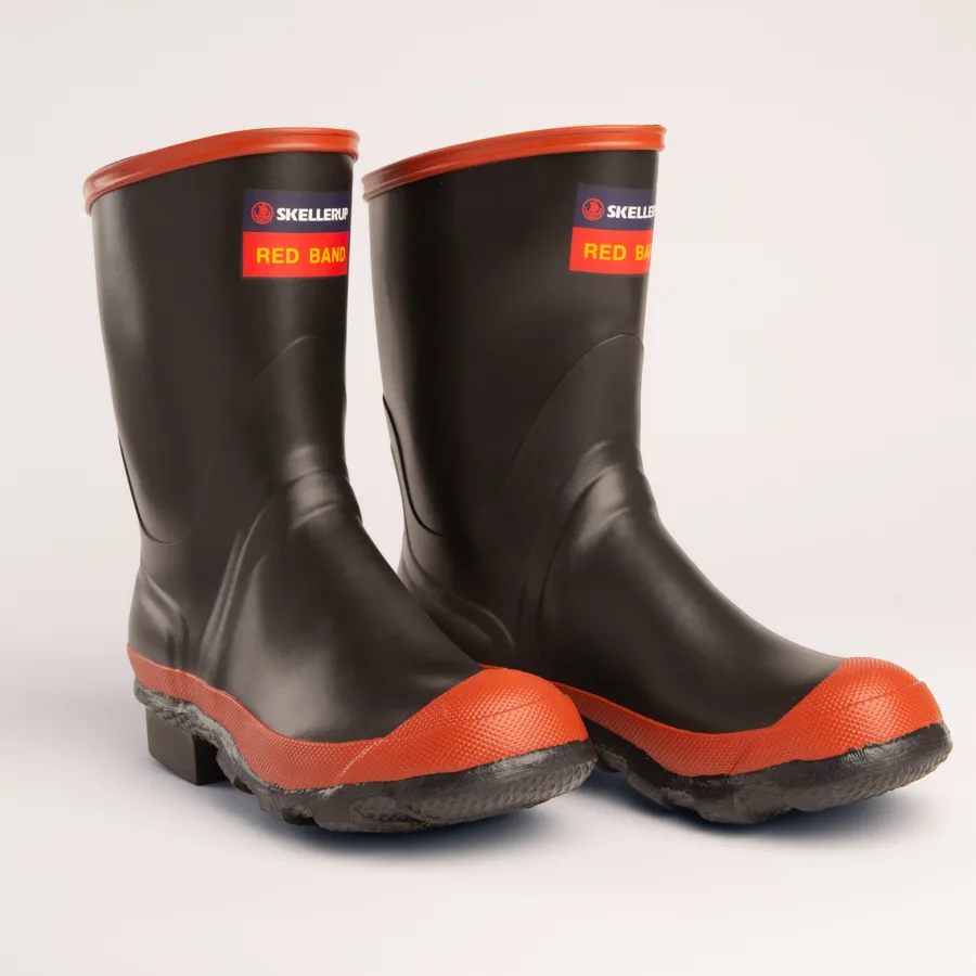A pair of black rubber boots with bright red bands around the soles and tops. The boots have SKELLERUP RED BAND labels near the top front. They are clean and placed on a plain light background.